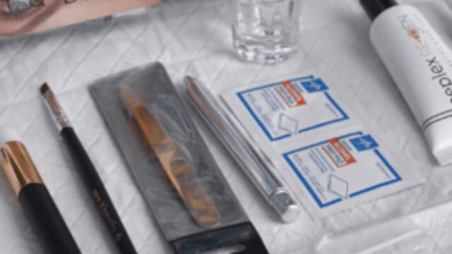 A collection of beauty tools and supplies, including makeup brushes, brow tint packaging, cleansing pads, and a small clear glass, arranged on a white surface.