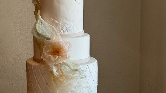 A four-tier white wedding cake with textured and floral decorations sits on a table. Two pieces are cut and are placed beside the cake along with a cake server.